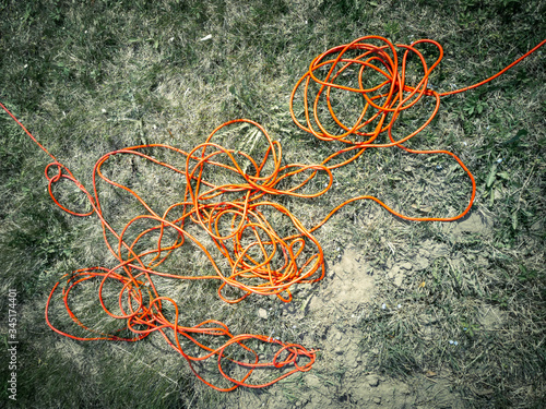 High contrast random chaotic wire harness of bright red electricity extension cable on gray ground background in garden