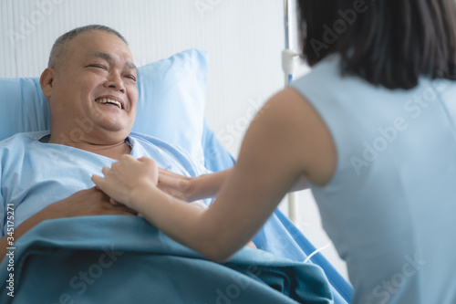 Cheerful asian nurse smiling and talking with elderly patient in the room.