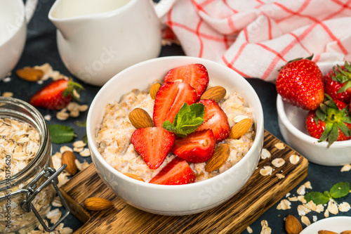 Oatmeal porridge with fresh strawberry and nuts on dark background.