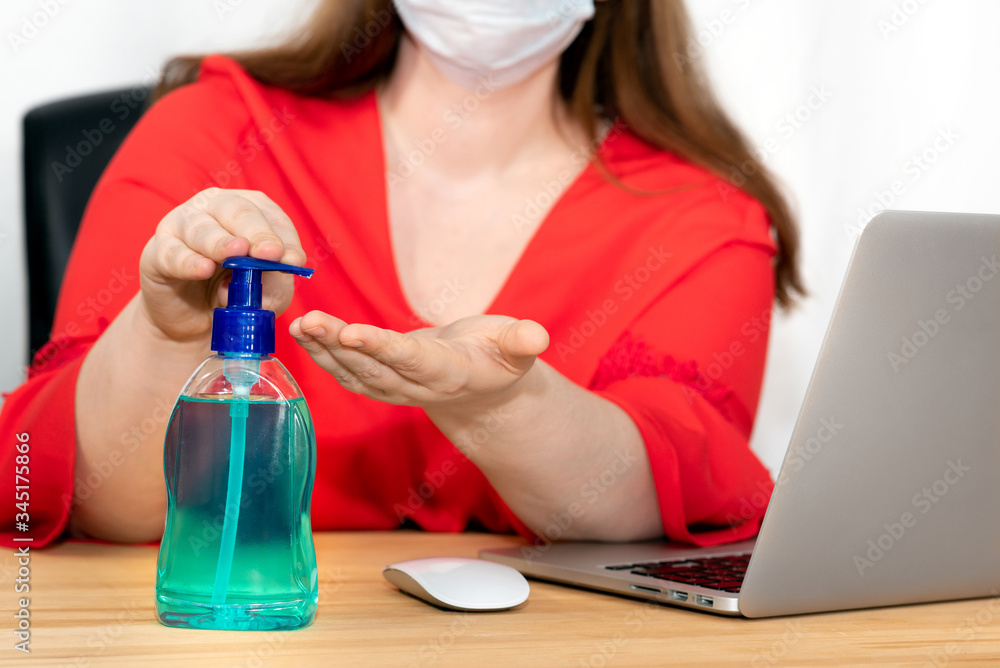 Woman working at the computer with a face mask disinfects her hands with hand sanitizer Woman working at the computer with a face mask disinfects her hands with hand sanitizer