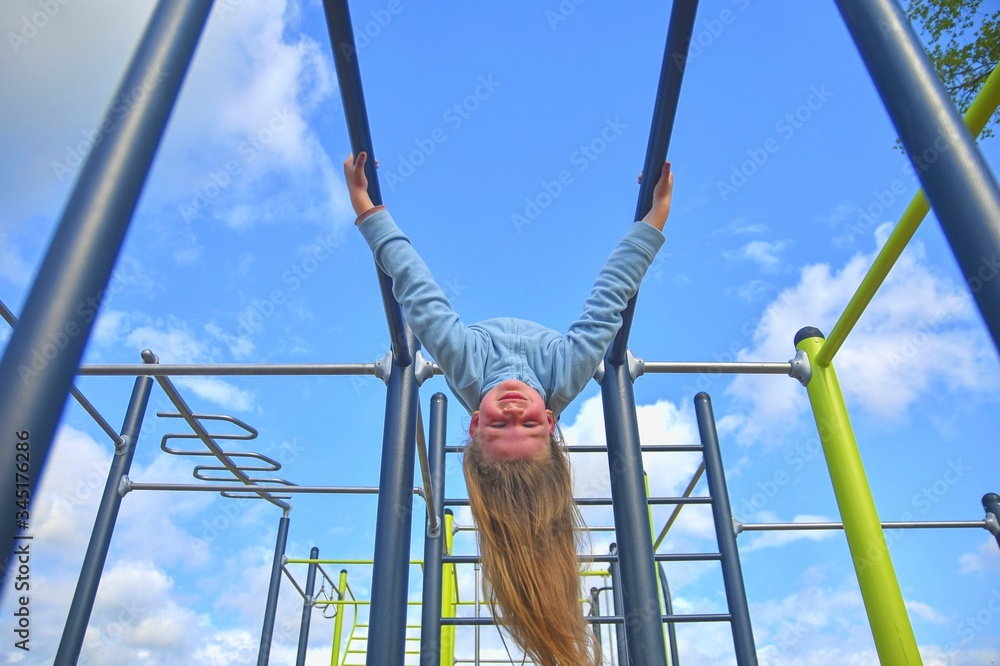 Fototapeta premium Little girl hanging upside down on parallel bars at playground.