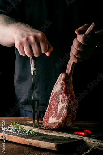 Obraz na plátně The chef's hands hold a raw Tomahawk a beef steak and a meat fork over a choppin