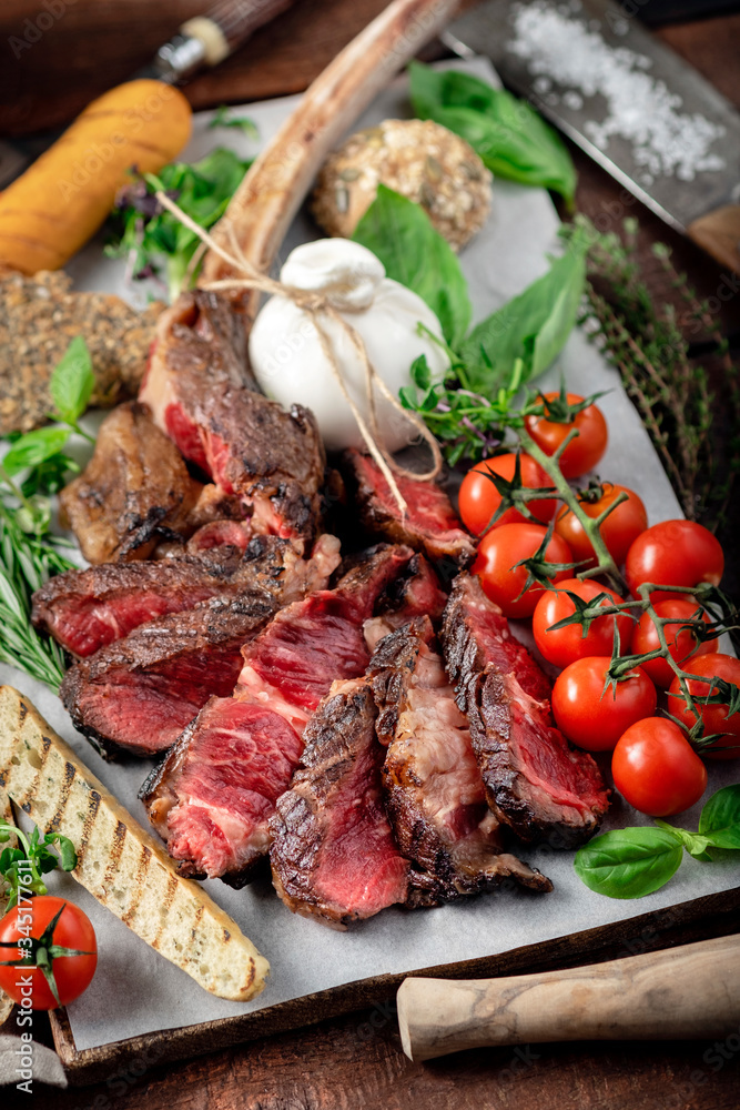 Tomahawk grilled steak cut into pieces with vegetables on a wooden Board, cooking meat barbecue Tomahawk grilled steak cut into pieces with vegetables on a wooden Board, cooking meat barbecue