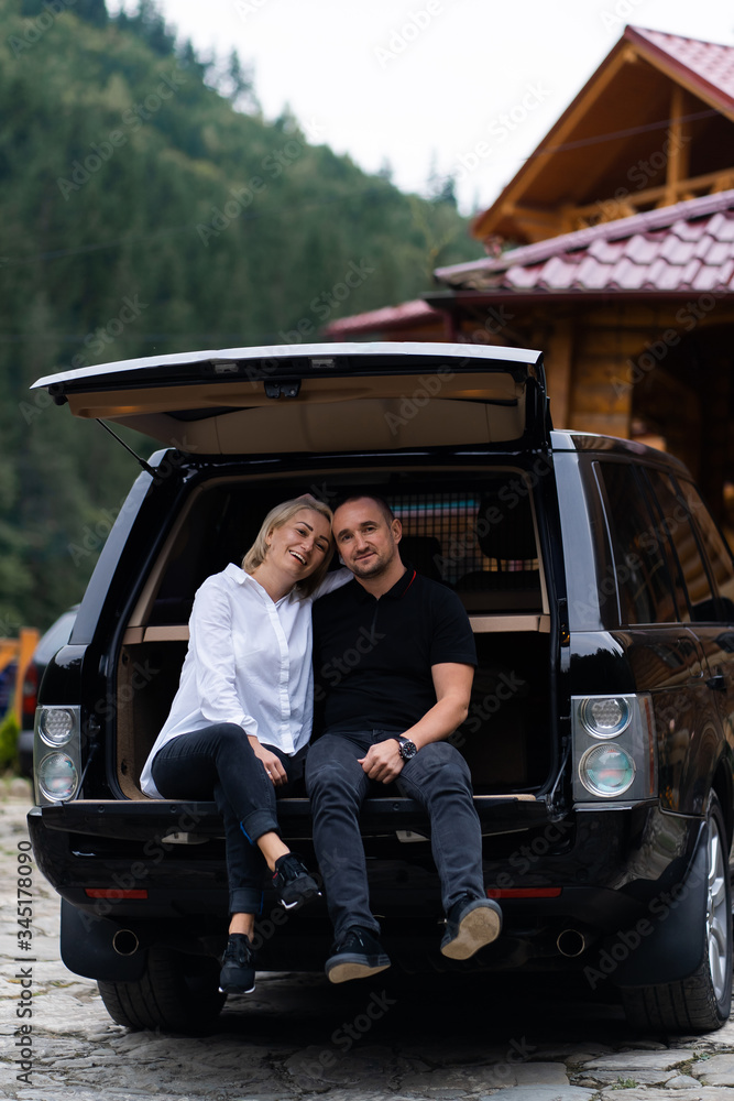 Portrait of beautiful sexy blonde woman and man sitting in luxury dark car . Fashion and business concept. Idea for couple photoshoot with car. Valentines day, surprise.