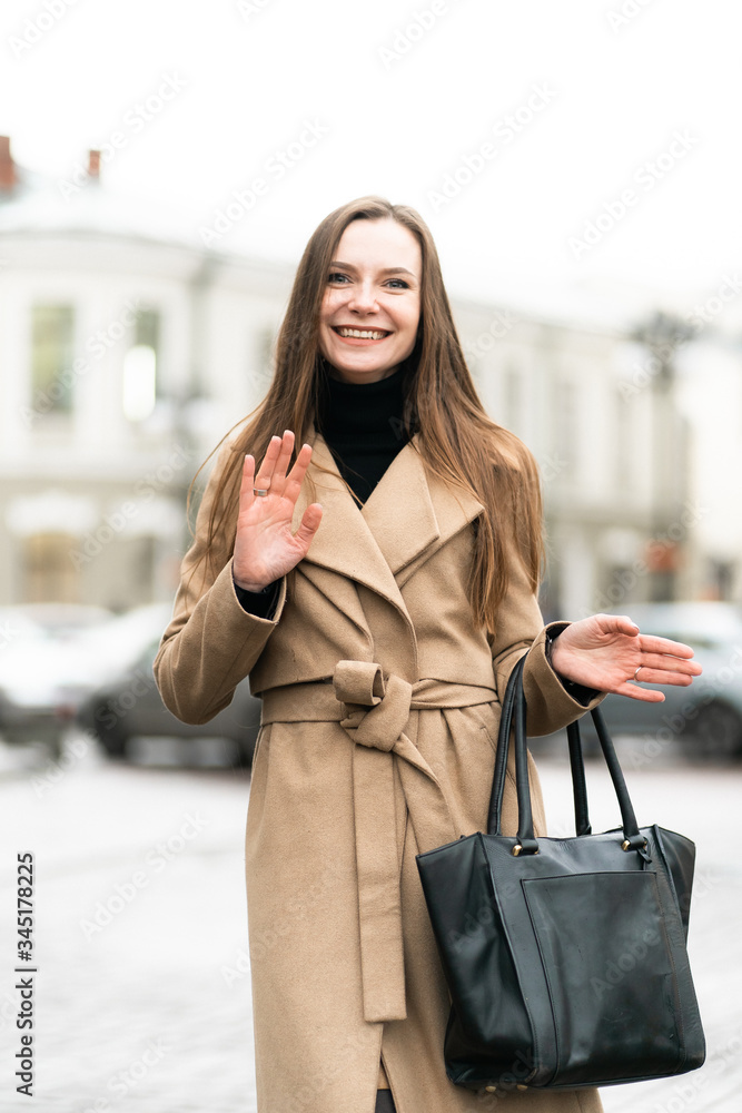 Outdoor fashion portrait of stylish young woman having fun, emotional face , laughing, Urban city street style wearing dark casual trousers, white sweater,creamy coat. and sunglasses Fashion concept.