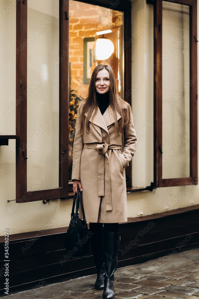 Outdoor fashion portrait of stylish young woman having fun, emotional face , laughing, Urban city street style wearing dark casual trousers, white sweater,creamy coat. and sunglasses Fashion concept.