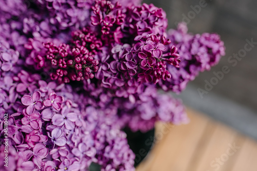 Close-up of a metallic bucket with a bunch of purple lilac flowers on a wooden bench.