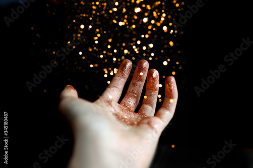 Hand in bronze sparkling glitter on dark background with falling glitter from the top © vladimirovna