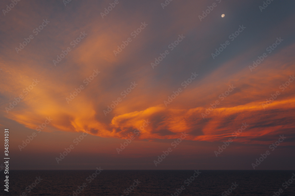 Moon rising over the sea and awesome orange-colored clouds after sunset, Adriatic sea, Italy