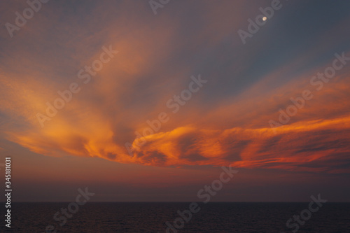 Moon rising over the sea and awesome orange-colored clouds after sunset, Adriatic sea, Italy
