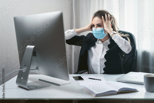 Alarmed young woman works in a home office during quarantine due to the pandemic of the coronavirus Covid-19. Girl in a disposable medical facial mask. Self-isolation to prevent infection