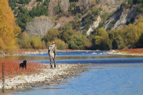 Man and black Labrador fishing on a New Zealand river in the autumn