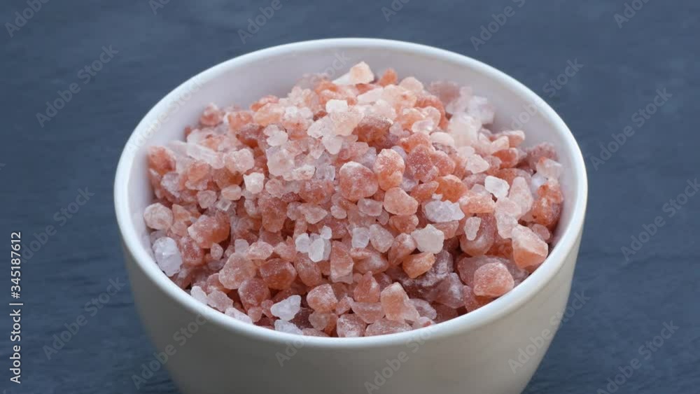 Close-up of white bowl with pink Himalayan salt on natural stone background. Close-up of white bowl with pink Himalayan salt on natural stone background.