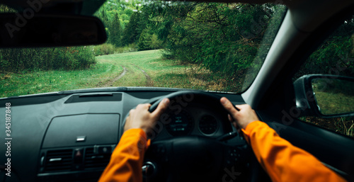 Driver dressed bright orange jacket driving a modern off road right hand drive RHD car on the mountain green forest country road. POV inside car windscreen view point. Safely auto driving concept. photo