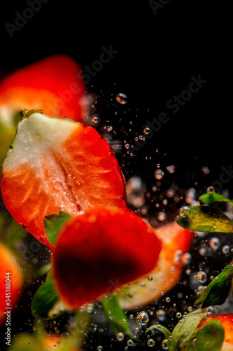 Closeup of fresh and healthy strawberries falling into clear water with big splash on black background. Group of juicy strawberries falling into water with splash. Red strawberries drop in water © Epic Vision