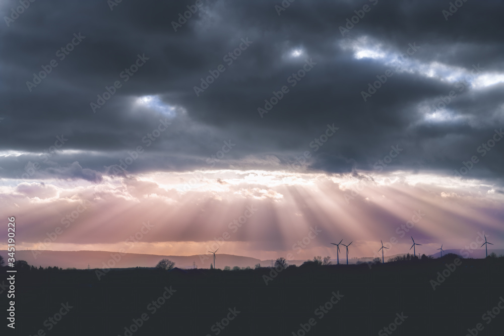 A dark cloud cover in the sky and sunbeams pouring out on the landscape