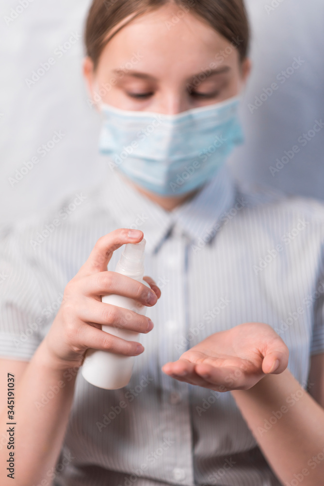 teenager girl of 11-14 years old, in medical mask covers face, holds an antiseptic spray in hand, disinfects hands from viruses bacteria, COVID-19 epidemic pandemic virus outbreak protection concept. teenager girl of 11-14 years old, in medical mask covers face, holds an antiseptic spray in hand, disinfects hands from viruses bacteria, COVID-19 epidemic pandemic virus outbreak protection concept.