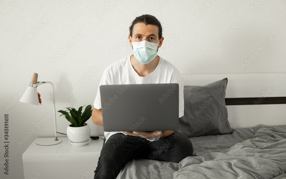 Man in medical mask is working from home with a laptop because of coronavirus epidemic. Remote work during pandemic. Stay home during COVID-19 quarantine concept. Freelancer. Man in medical mask is working from home with a laptop because of coronavirus epidemic. Remote work during pandemic. Stay home during COVID-19 quarantine concept. Freelancer.