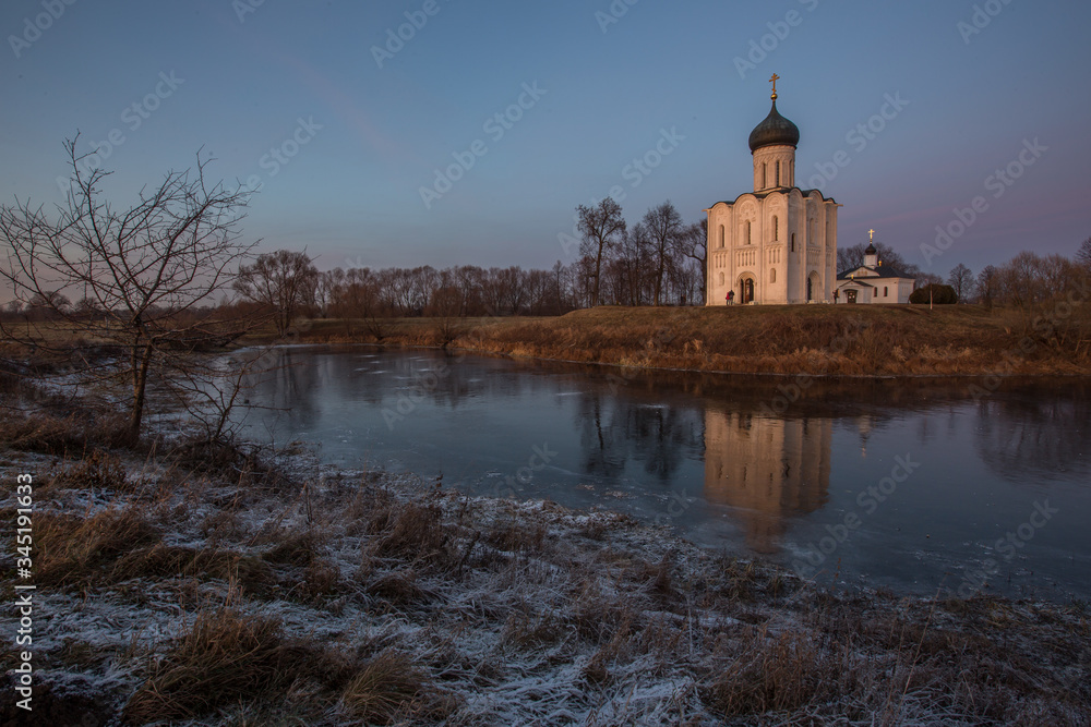 A beautiful temple on a background of bright golugobo sky stands on the shore of a lake is reflected in the ice at sunset