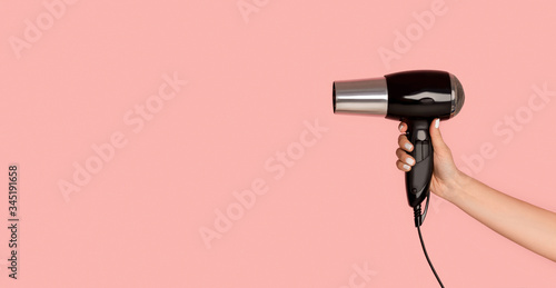 Unrecognizable girl showing hairdryer on pink background, empty space. Panorama photo