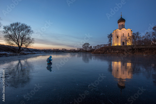 A beautiful temple against the bright blue sky stands on the lake, the temple is reflected in the ice of the lake, in front of the temple on the ice a girl stands on her knees and takes pictures