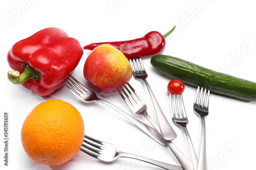 close up of fresh cherry tomato, red peppers, cucumber, apple and orange fruits on forks on white background. Healthy eating and vegetarian food, cooking concept.