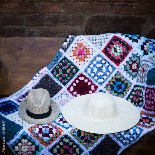 a nice pair of hats and a handmade colorful blanket on a bench in the garden