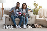Young Black Couple Sitting Beside Folded Clothes And Shoes At Home