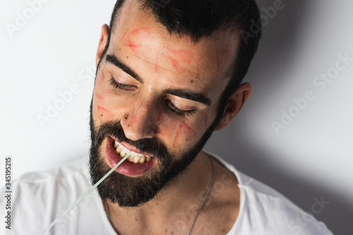 Bild auf Leinwand Seductive man with traces of lipstick on his face playing with a bubble gum