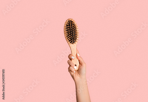 Closeup of millennial girl holding wooden hairbrush on pink background photo