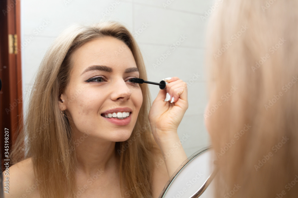 Beautiful girl paints eyelashes in the bathroom.