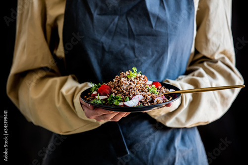 woman in an apron holds a plate of buckwheat in her hands