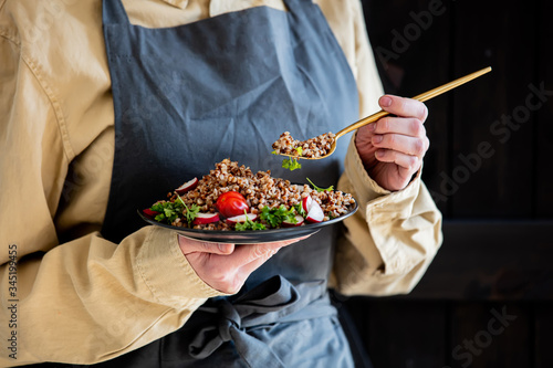 woman in an apron holds a plate of buckwheat in her hands