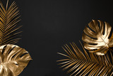 Gold painted tropical leaves on black plain paper background.