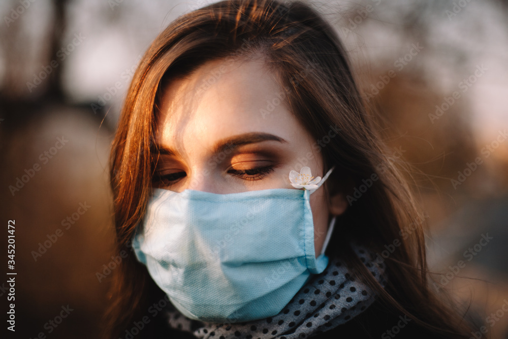 Close up portrait of sad teenage girl wearing protective face medical mask standing outdoors in park during spring Close up portrait of sad teenage girl wearing protective face medical mask standing outdoors in park during spring