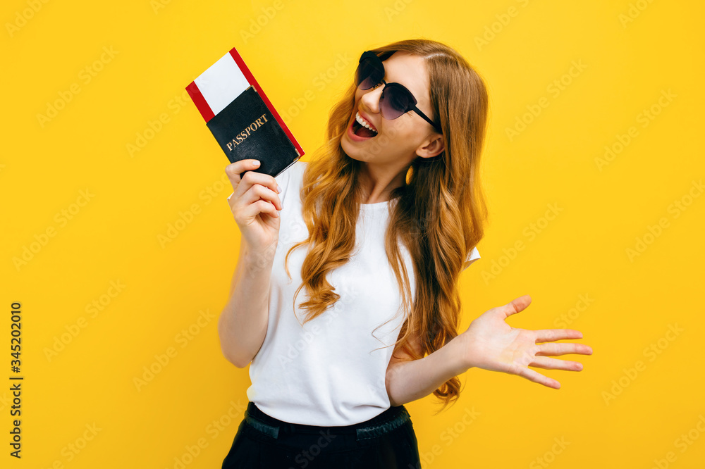 Naklejka premium beautiful woman with dark glasses holding a passport and tickets on a yellow background. The concept of travel, business