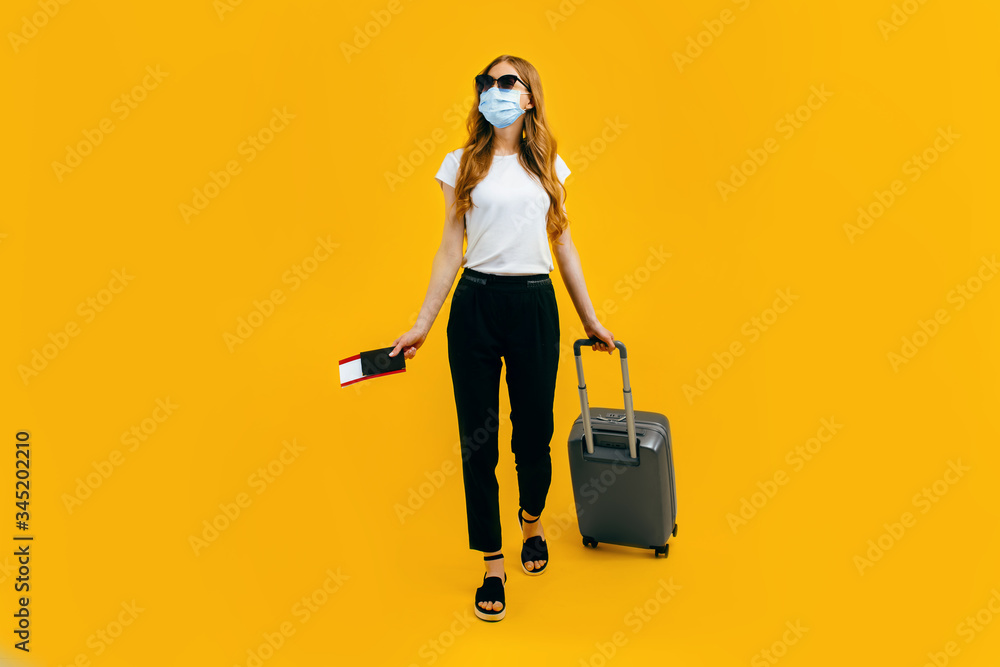 A female passenger in a medical protective mask on her face, with a suitcase and passport, goes abroad. Concept of travel, quarantine and coronavirus A female passenger in a medical protective mask on her face, with a suitcase and passport, goes abroad. Concept of travel, quarantine and coronavirus