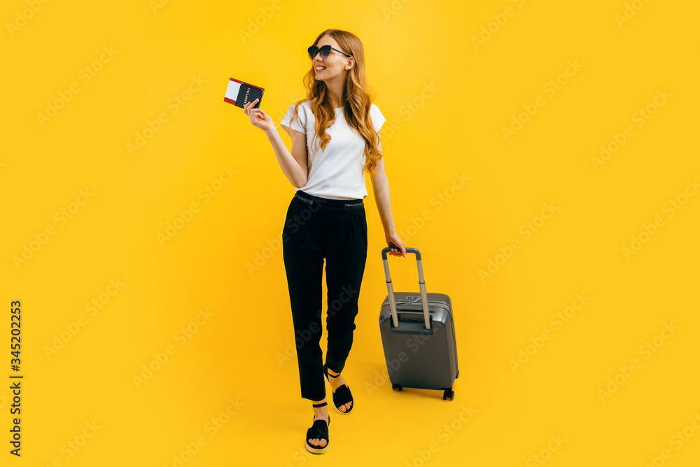 Happy beautiful woman, with a suitcase and passport with tickets on a yellow background. The concept of travel, business Happy beautiful woman, with a suitcase and passport with tickets on a yellow background. The concept of travel, business