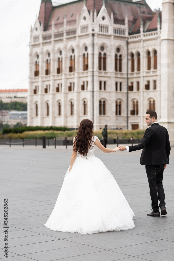 Bride and groom dancing in the old town street. Wedding couple walks in Budapest near Parliament House. Caucasian happy romantic young couple celebrating their marriage. Wedding and love concept. Bride and groom dancing in the old town street. Wedding couple walks in Budapest near Parliament House. Caucasian happy romantic young couple celebrating their marriage. Wedding and love concept.