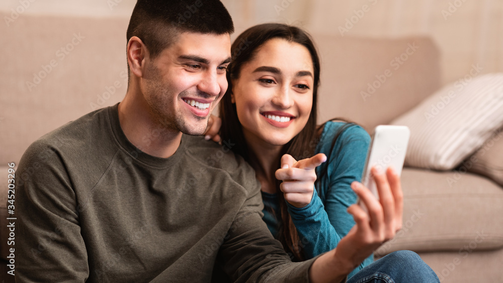 Couple using cell phone sitting on floor, free space Couple using cell phone sitting on floor, free space