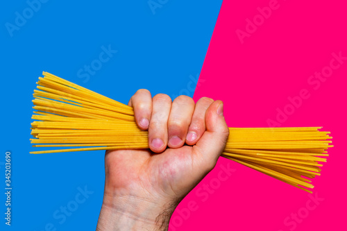 hand holding serving of raw spaghetti pasta on blue and pink background - energy of carbohydrates and sugars
