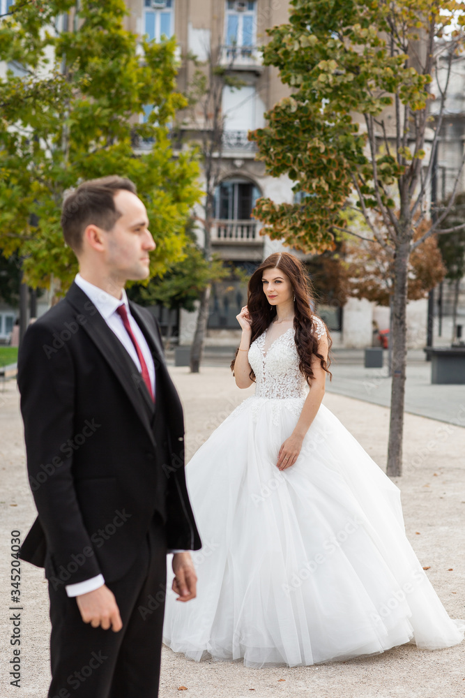 Fototapeta premium Bride and groom dancing in the old town street. Wedding couple walks in Budapest near Parliament House. Caucasian happy romantic young couple celebrating their marriage. Wedding and love concept.
