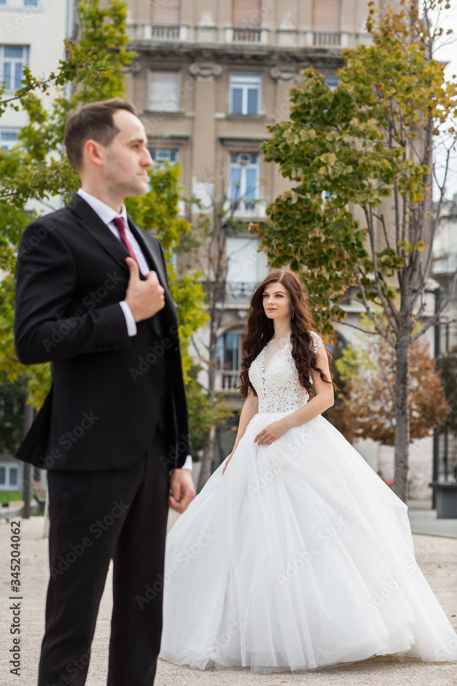 Fototapeta premium Bride and groom dancing in the old town street. Wedding couple walks in Budapest near Parliament House. Caucasian happy romantic young couple celebrating their marriage. Wedding and love concept.