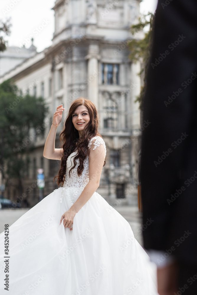 Naklejka premium Bride in the old town street. Wedding walks in Budapest near Parliament House. Caucasian happy romantic young woman celebrating her marriage. Wedding and love concept.