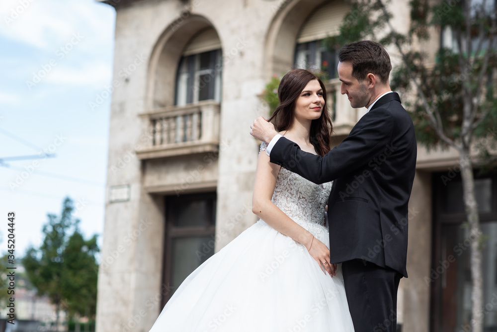 Bride and groom hugging in the old town street. Wedding couple walks in Budapest near Parliament House. Caucasian happy romantic young couple celebrating their marriage. Wedding and love concept.