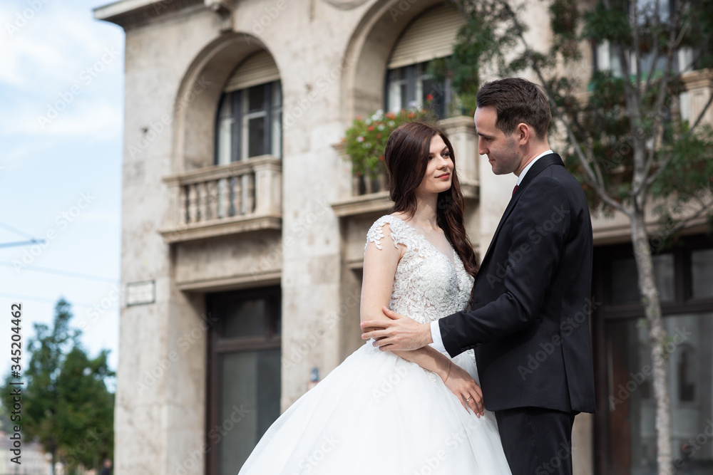 Bride and groom hugging in the old town street. Wedding couple walks in Budapest near Parliament House. Caucasian happy romantic young couple celebrating their marriage. Wedding and love concept.