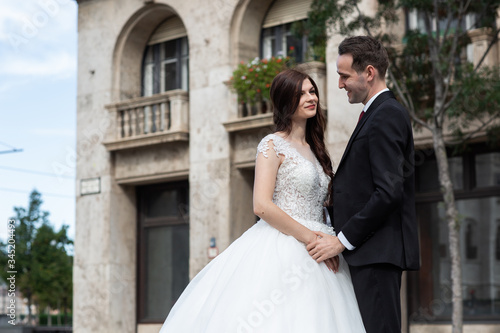 Bride and groom hugging in the old town street. Wedding couple walks in Budapest near Parliament House. Caucasian happy romantic young couple celebrating their marriage. Wedding and love concept.