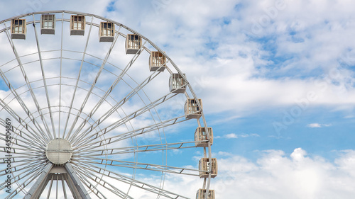 ferris wheel for family holidays with cabs design of white color against the sky with clouds and nobody, side view copy space.