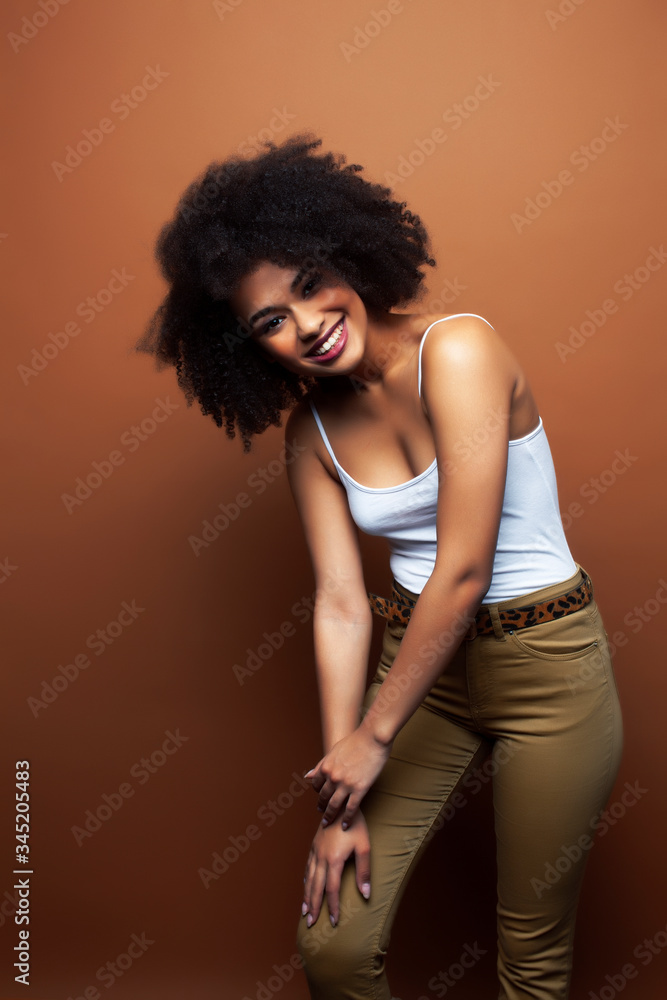 pretty young african american woman with curly hair posing cheerful gesturing on brown background, lifestyle people concept pretty young african american woman with curly hair posing cheerful gesturing on brown background, lifestyle people concept
