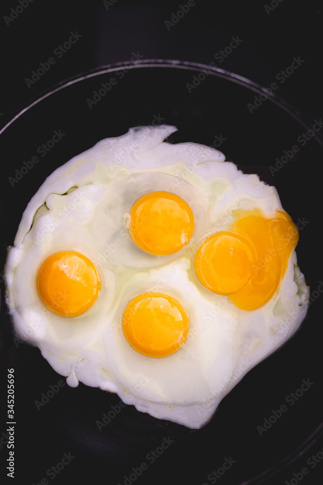 Fried eggs in frying pan. Four eggs. Making breakfast for family. Family weekend breakfast. Quick easy brunch breakfast. Over medium fried eggs. Egg yolk, egg whites. Black stove top. Broken egg yolk Fried eggs in frying pan. Four eggs. Making breakfast for family. Family weekend breakfast. Quick easy brunch breakfast. Over medium fried eggs. Egg yolk, egg whites. Black stove top. Broken egg yolk